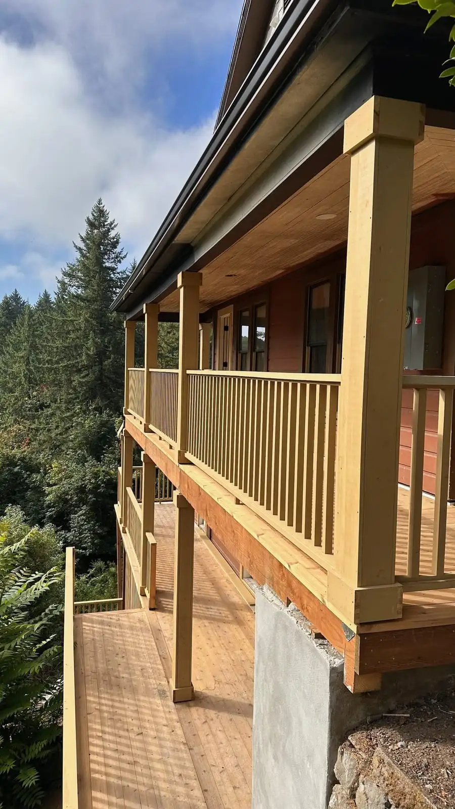 Elevated covered wood deck with stained railing on a hillside home