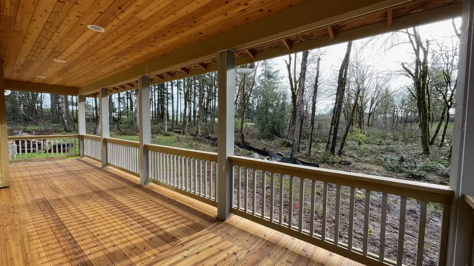 Covered wraparound cedar deck with white railing overlooking a wooded lot