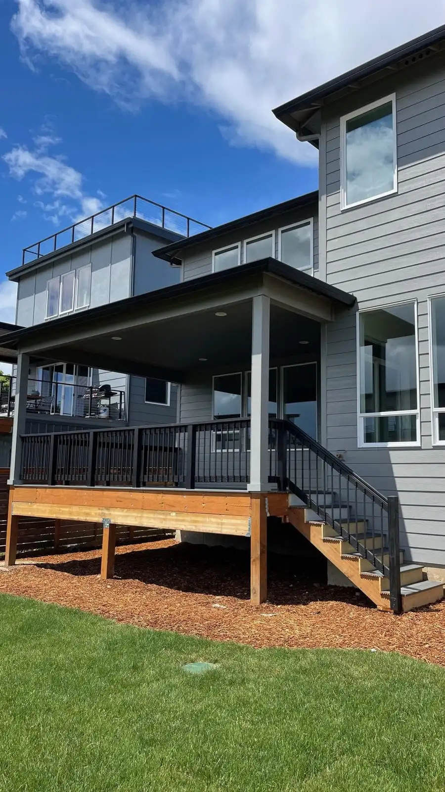Elevated wood deck with black railing and stairs on a modern home