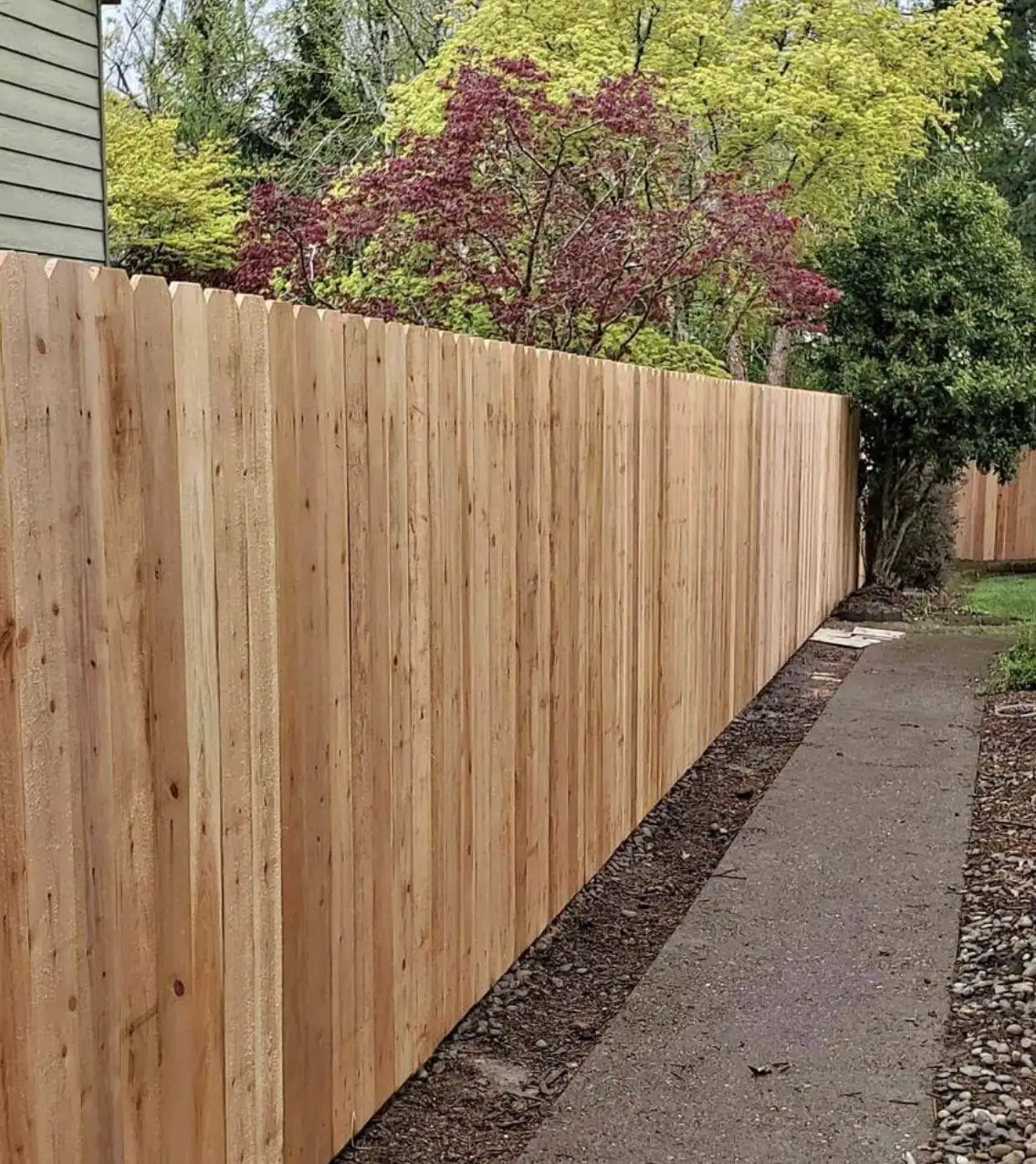 Horizontal cedar fence along a concrete walkway beside a light-sided house