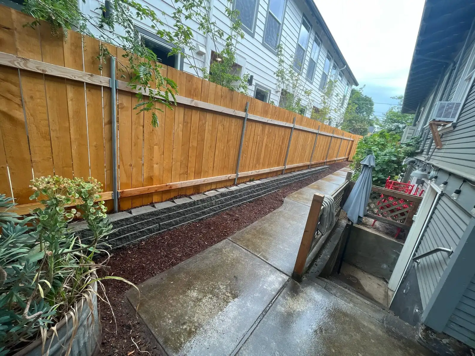 Cedar fence on a block retaining wall beside a concrete walkway