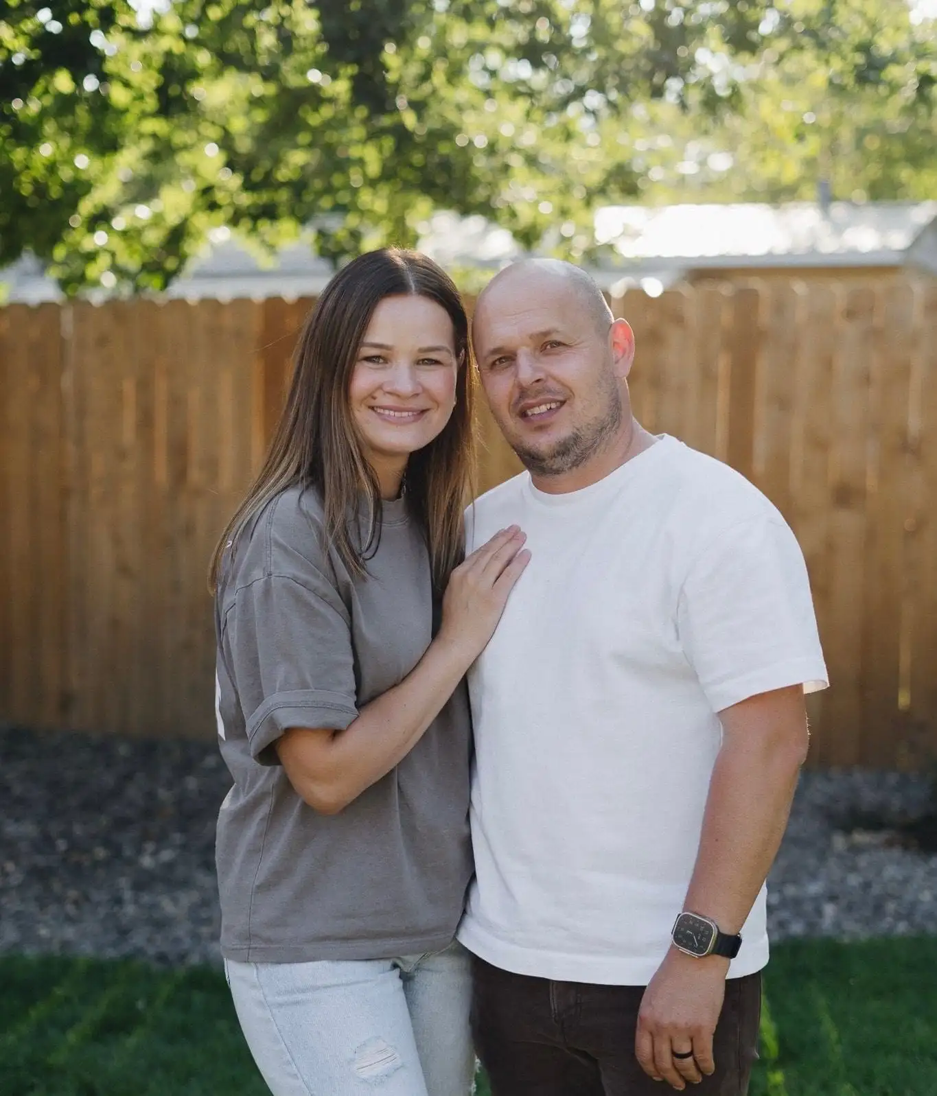 Smiling couple standing in front of a wood fence in a backyard